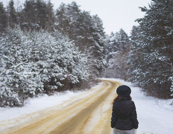 A beautiful snowy day, the girl stands with her back in the middle of the road in a pine forest.