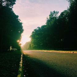 Road by trees on field against sky at sunset