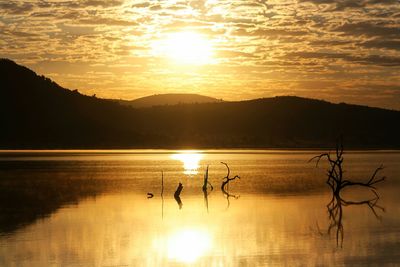 Silhouette people on lake against sky during sunset