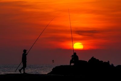 Silhouette man fishing in sea against sunset sky