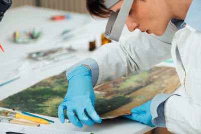 Female conservator with magnifying goggles cleaning dirt from antique oil painting