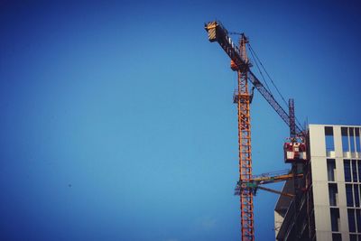 Low angle view of crane against clear blue sky