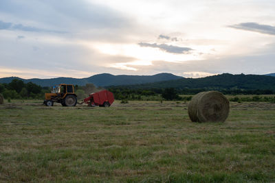 Tractor creating hay bales in the field during sunset