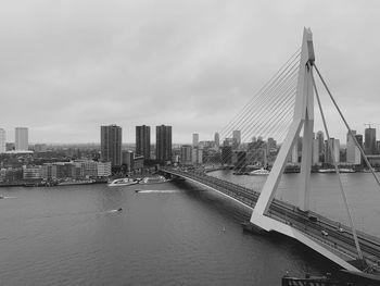 Bridge over river by city buildings against sky
