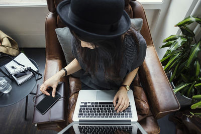 High angle view of female blogger using phone and laptop while sitting on chair