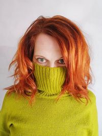 Portrait of mid adult woman with covering face with sweater while standing against wall