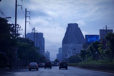 Cars on road by buildings in city against sky