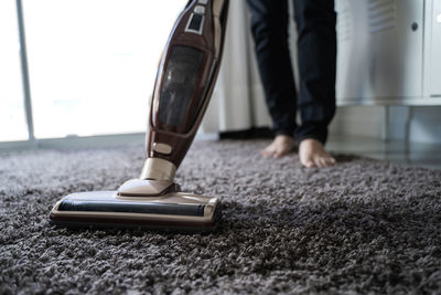 Low section of person cleaning rug with vacuum cleaner at home