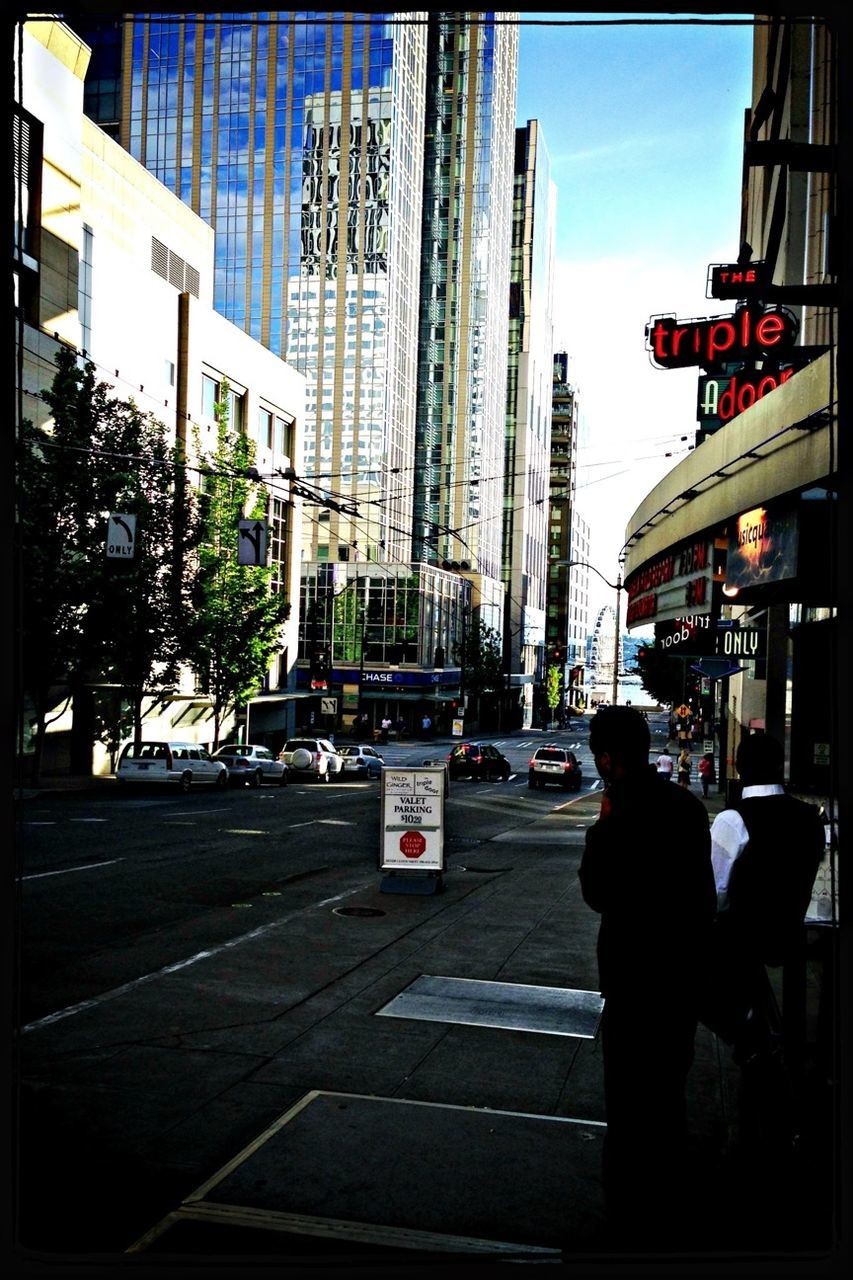 building exterior, architecture, city, built structure, street, city life, transportation, car, skyscraper, transfer print, sky, land vehicle, office building, city street, men, tall - high, incidental people, sunlight, tower, mode of transport