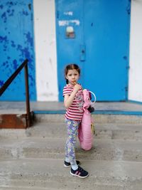 Full length of cute girl eating candy while standing on steps