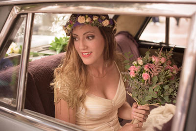 Smiling bride with flower bouquet sitting in car