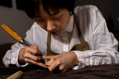 Young chinese female violin maker working with gouge to making a new violin in her workshop