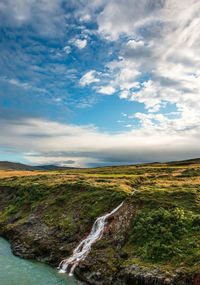 Scenic view of landscape with waterfall against sky