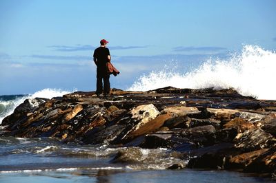 Man standing on rock by sea against sky