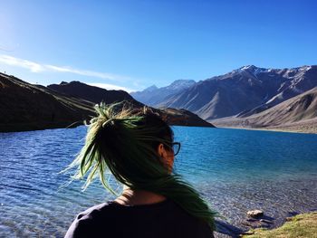 Rear view of woman looking at lake by mountains against blue sky