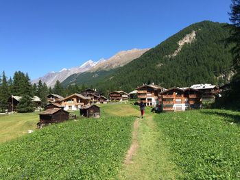 Rear view of woman walking on field in village at zermatt against clear sky