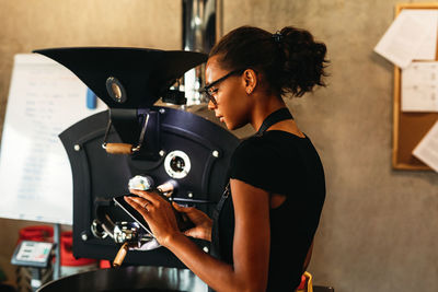 Side view of woman using digital tablet while standing by coffee maker