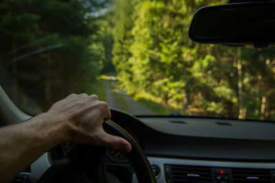 Cropped hand of man on steering wheel in car