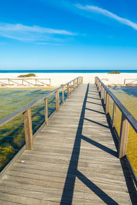 Boardwalk leading towards sea against blue sky