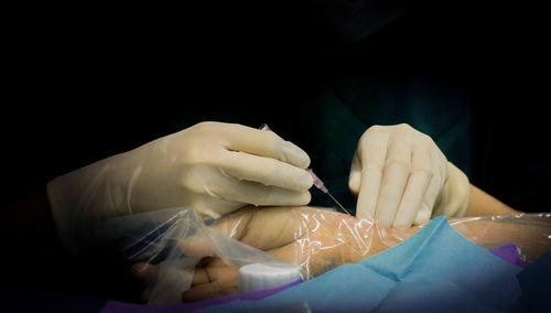 Cropped hands of doctor injecting patient against black background