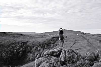 Rear view of man standing on rock against sky