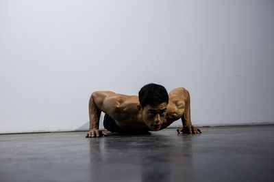 Shirtless man doing push-ups against wall