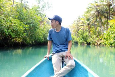 Young man looking at river while sitting in boat against trees