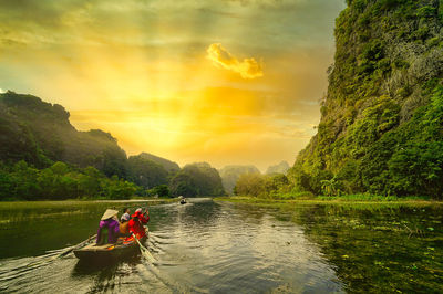 People on river against sky during sunset