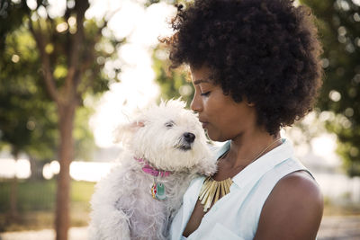 Woman with curly hair kissing dog while standing at park