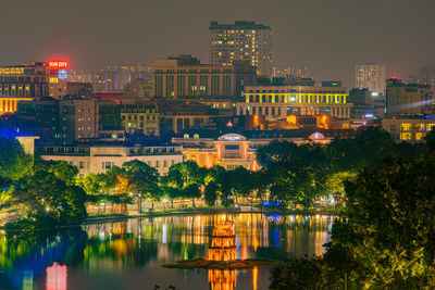 Illuminated buildings by river against sky at night