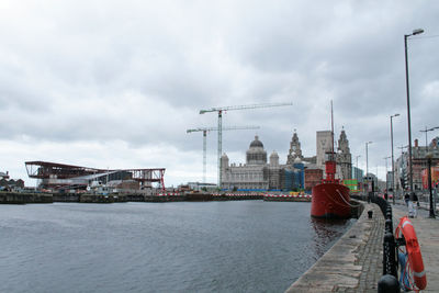 Sea by buildings against cloudy sky