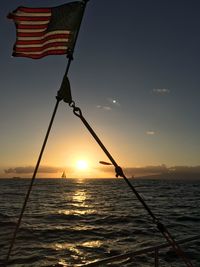 American flag on boat in sea against sky during sunset