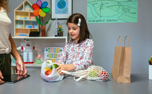 Student taking fruits from disposable plastic bag to reusable mesh bag in ecology classroom