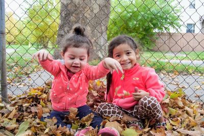 Sisters playing with autumn leaves against fence in park