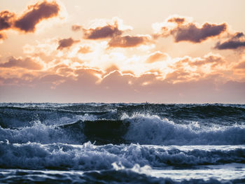 Sea waves rushing towards shore against sky during sunset