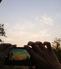 Midsection of man holding camera against sky during sunset