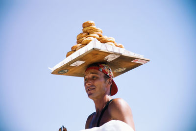 Man balancing tray of bread against clear sky