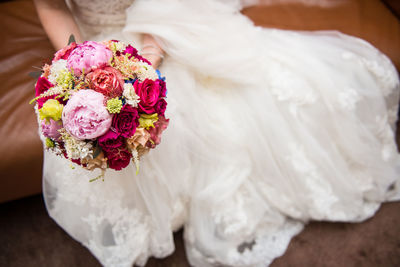 Low section of bride wearing wedding dress with bouquet