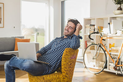 Portrait of smiling young man sitting on armchair in the living room with laptop