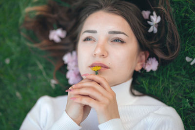 Close-up of thoughtful beautiful woman holding flower while lying on grass
