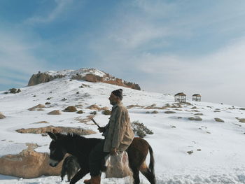 Person riding horse on snow covered mountain against sky