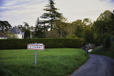 Road sign by trees against sky