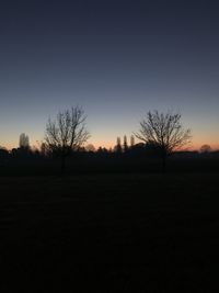 Silhouette bare trees on field against clear sky at sunset