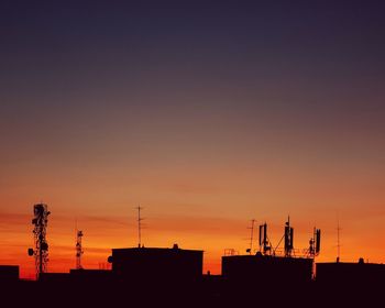 Silhouette antennas over buildings against sky during sunset