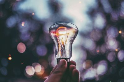 Cropped image of hand holding illuminated light bulb during sunset