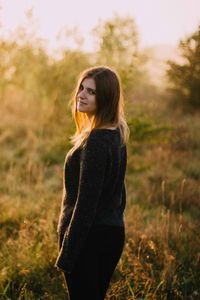 Portrait of young woman standing on field during sunset