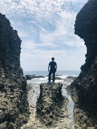 Rear view of man standing on rock by sea against sky
