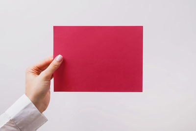 Cropped hand of woman holding paper against blue background