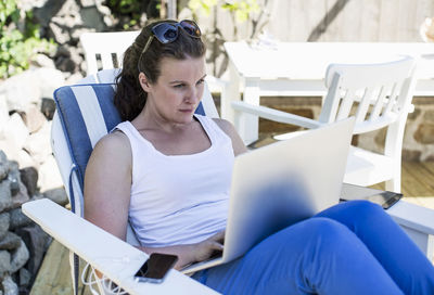 Mid adult woman using laptop on lounge chair at yard