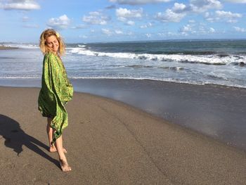 Woman with green sarong standing on shore at beach against sky during sunny day